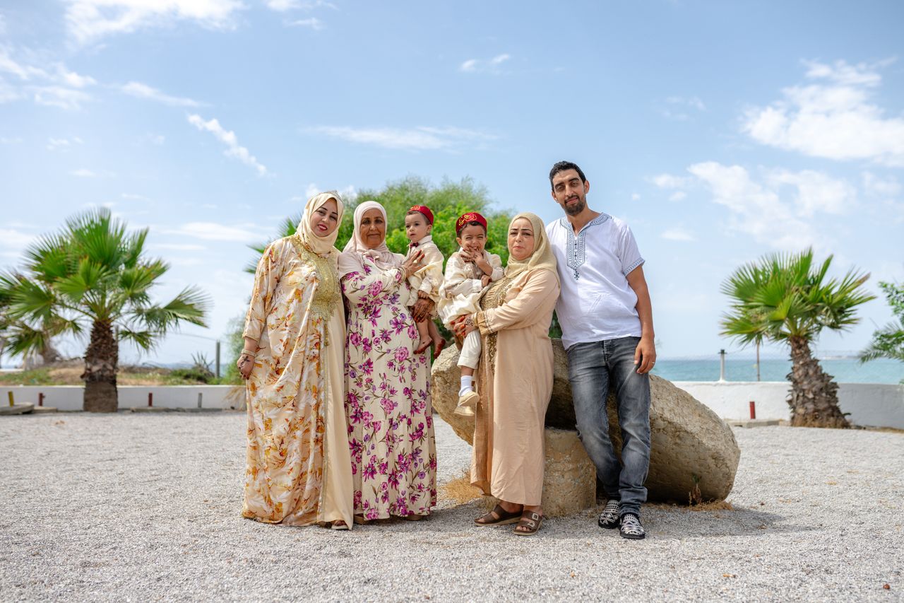 Tunisian family in traditional dress posing near the Mediterranean coast at Nabeul, Tunisia, with palm trees and calm sea behind