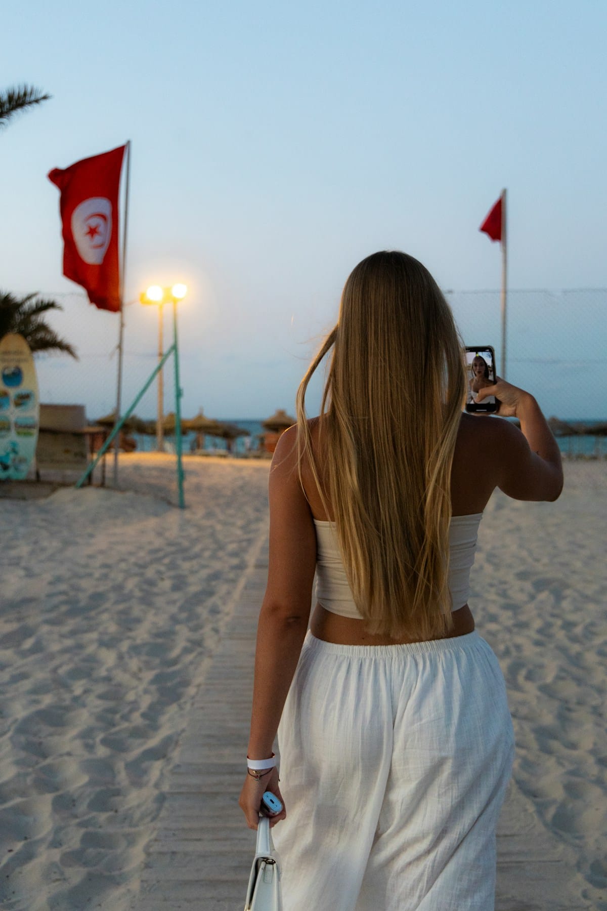 A tourist on a Tunisian beach at dusk, with the Tunisian flag visible in the background