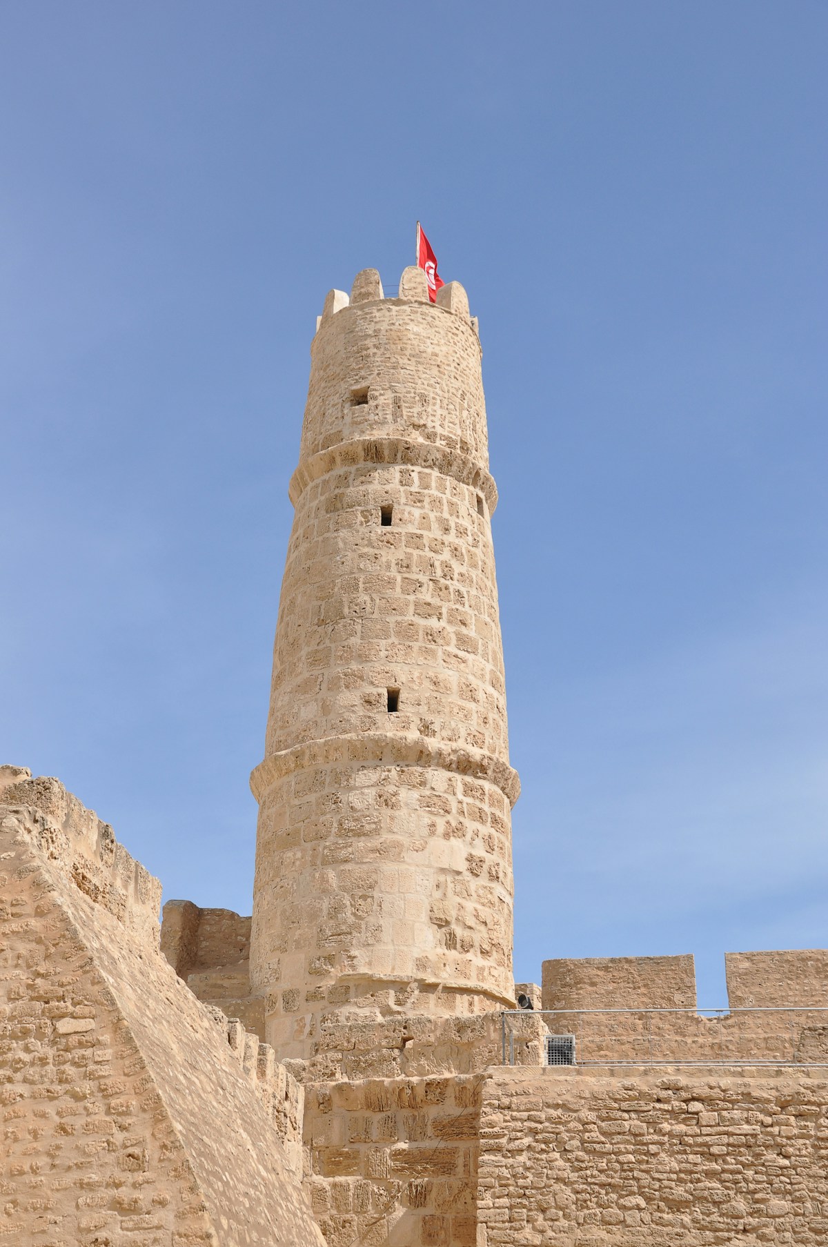 The watchtower of the Ribat of Monastir with Tunisian flag against a clear blue sky
