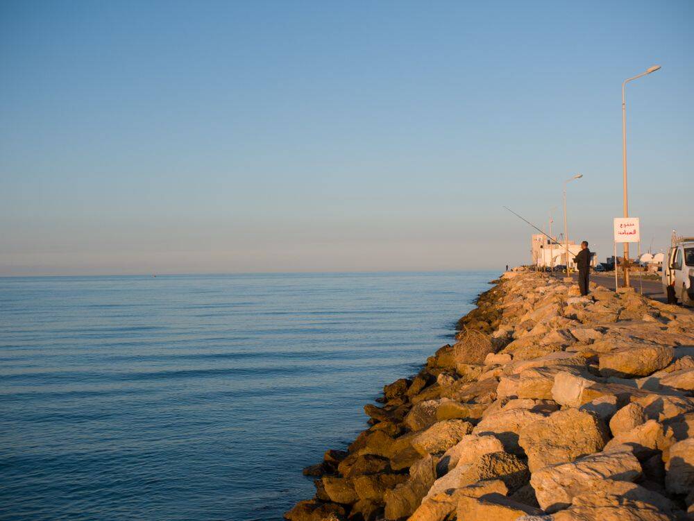 Pêcheur sur la côte rocheuse de Gabès au lever du soleil, Tunisie