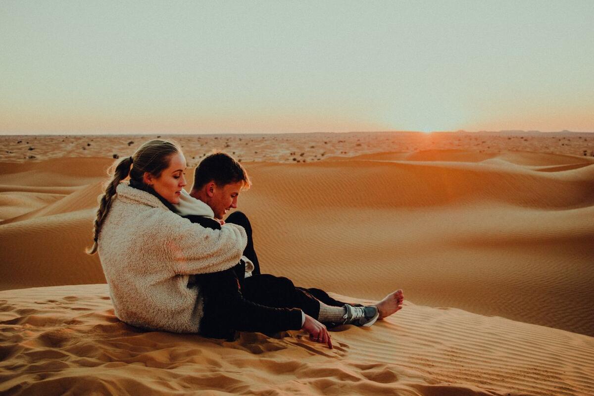 Couple watching the sun set over Sahara dunes in Tunisia